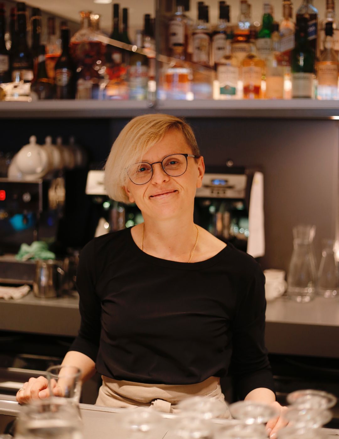 Smiling staff member standing behind the library bar at the ambassade hotel.
