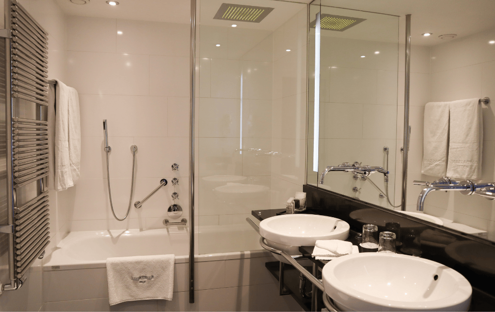 Badezimmer mit Doppelwaschbecken, Dusche in der Badewanne und WC im Ambassade Hotel.