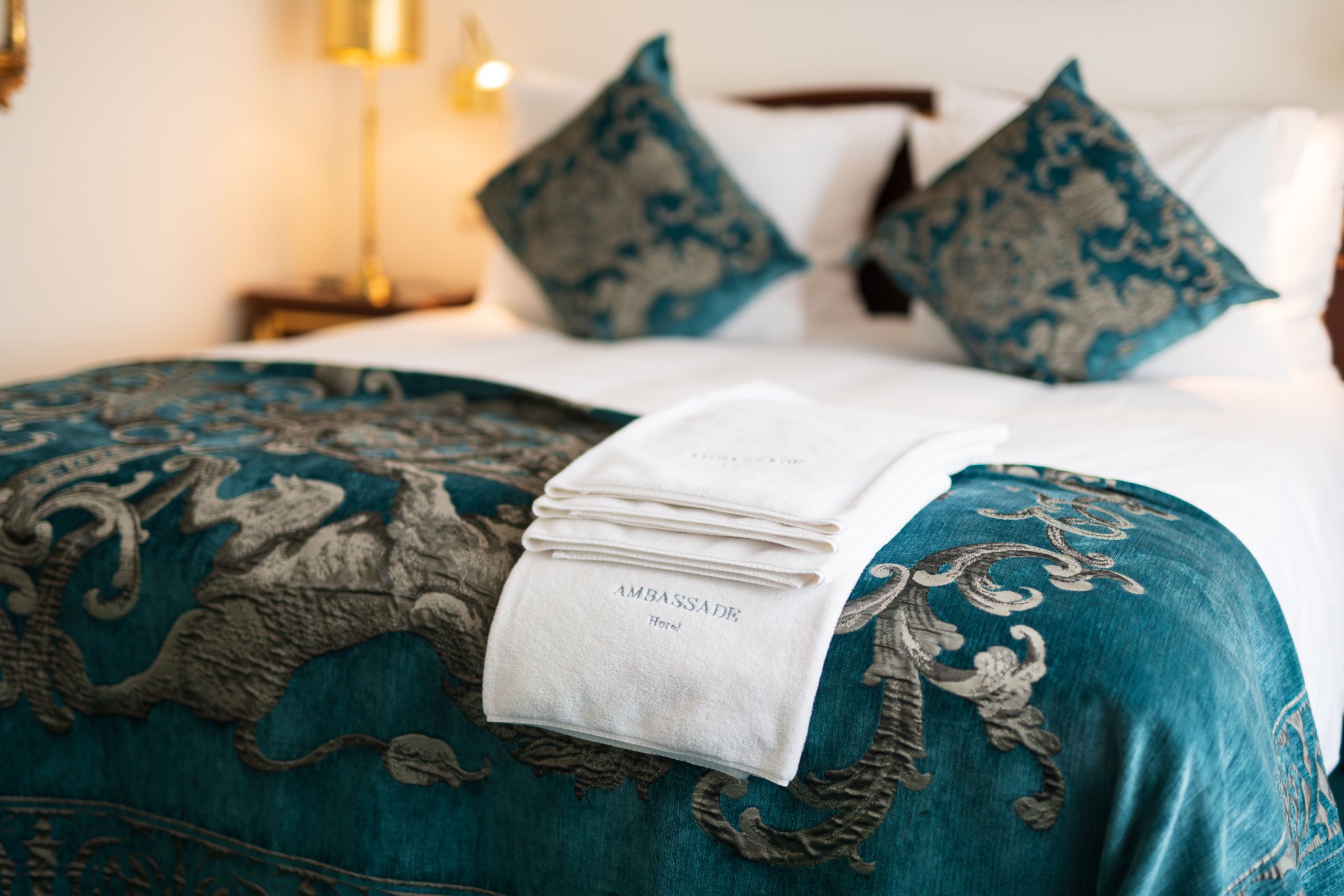 Soft, neatly folded towels placed on a hotel bed at the ambassade hotel, ready for guest use.