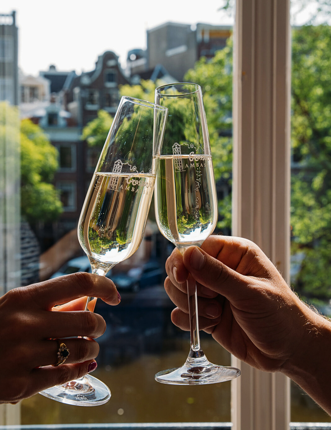 Deux verres de cava trinquant dans une chambre avec vue sur le canal à l'hôtel Ambassade à Amsterdam.