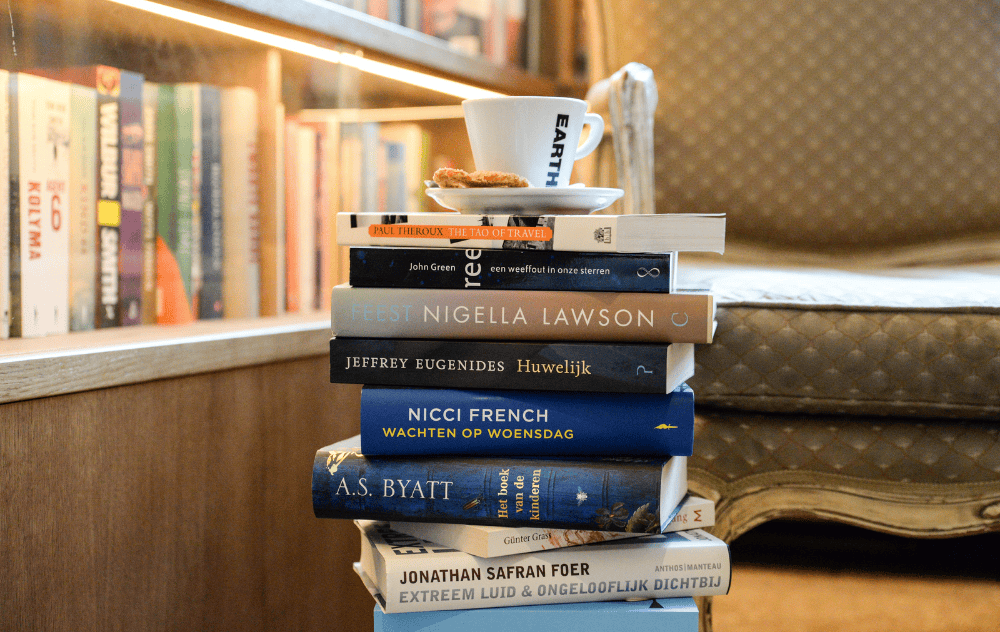 Pile de livres avec une tasse de café à l’Hôtel Ambassade à Amsterdam, reflétant l’ambiance d’un véritable hôtel littéraire.