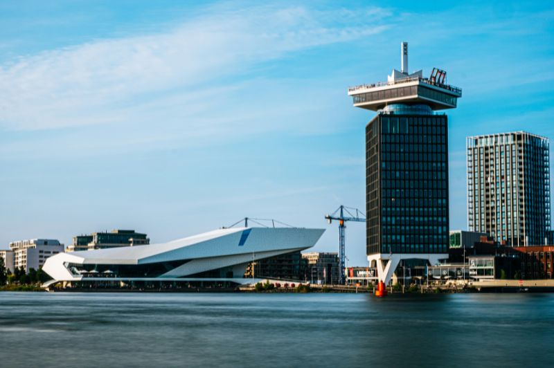 Vue sur la rivière IJ à Amsterdam avec des bateaux et des bâtiments au bord de l’eau.