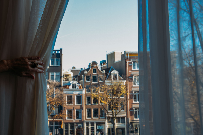 Un client ouvre les rideaux dans une chambre de l’Hôtel Ambassade à Amsterdam, dévoilant une vue sur les maisons de canal historiques.