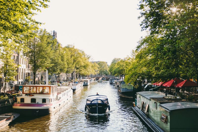 Bateau naviguant le long d’un canal d’Amsterdam bordé de bâtiments historiques.
