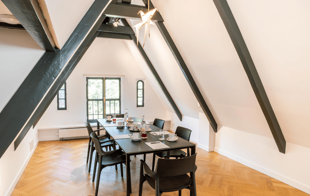Disposition de table de réunion dans le grenier de l’hôtel Ambassade, un espace élégant et privé avec un charme historique.