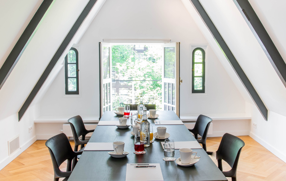 Espace de réunion lumineux dans le grenier de l’hôtel Ambassade avec portes ouvertes et lumière naturelle.