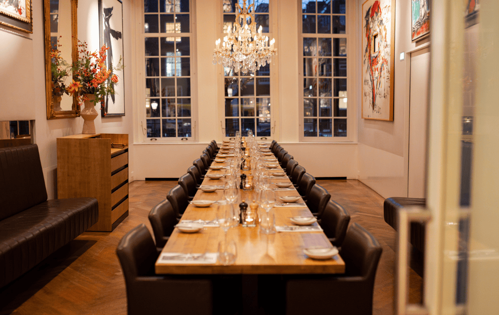 Lounge Wolvecamp à la Brasserie Ambassade à Amsterdam aménagée pour un dîner privé, avec une longue table et de grandes fenêtres laissant entrer la lumière naturelle.