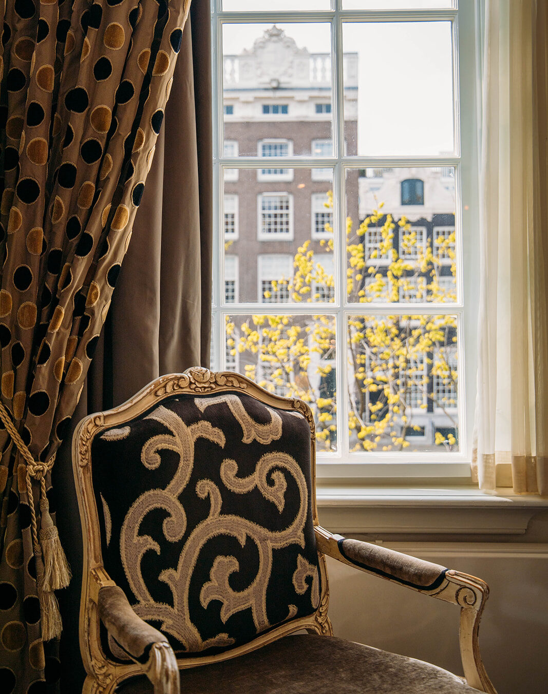 Fauteuil élégant près de la fenêtre avec vue sur le canal dans une chambre de l’Ambassade Hotel à Amsterdam.