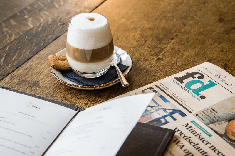 Tasse de café avec un journal et un menu sur la table.