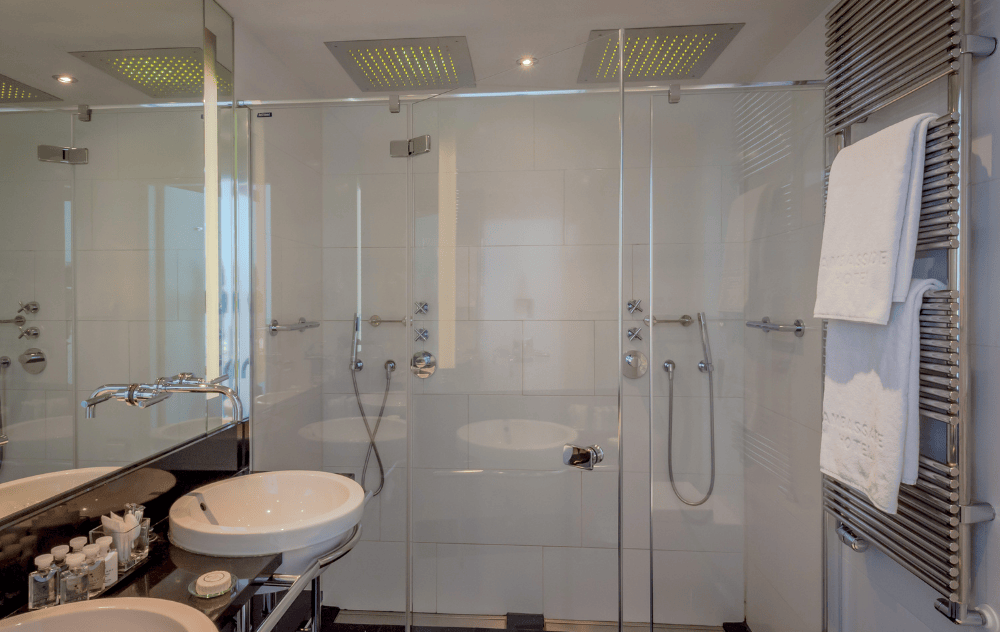 Salle de bains avec double vasque et deux douches à effet pluie à l’Ambassade Hotel.