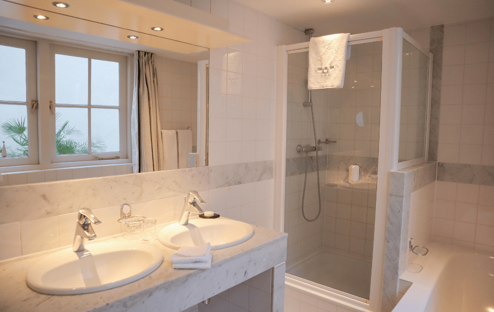 Salle de bains avec double vasque, douche séparée et baignoire à l’Ambassade Hotel.