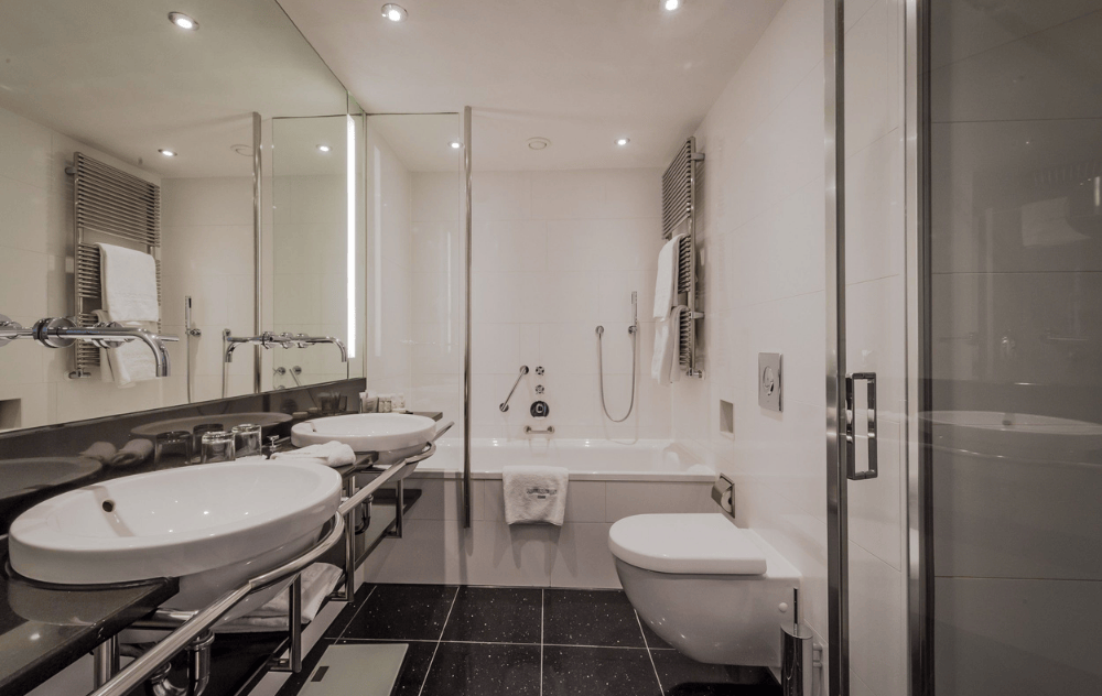 Salle de bains avec double vasque, douche dans la baignoire et toilettes à l’Ambassade Hotel.
