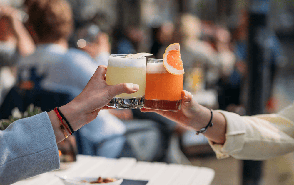 Deux invités trinquant avec des cocktails sur la terrasse de l’hôtel Ambassade.