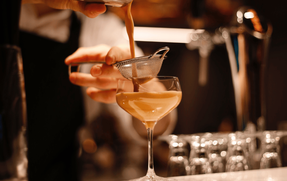 Barman versant un cocktail fraîchement secoué à travers une passoire dans le Library Bar de l’Hôtel Ambassade.
