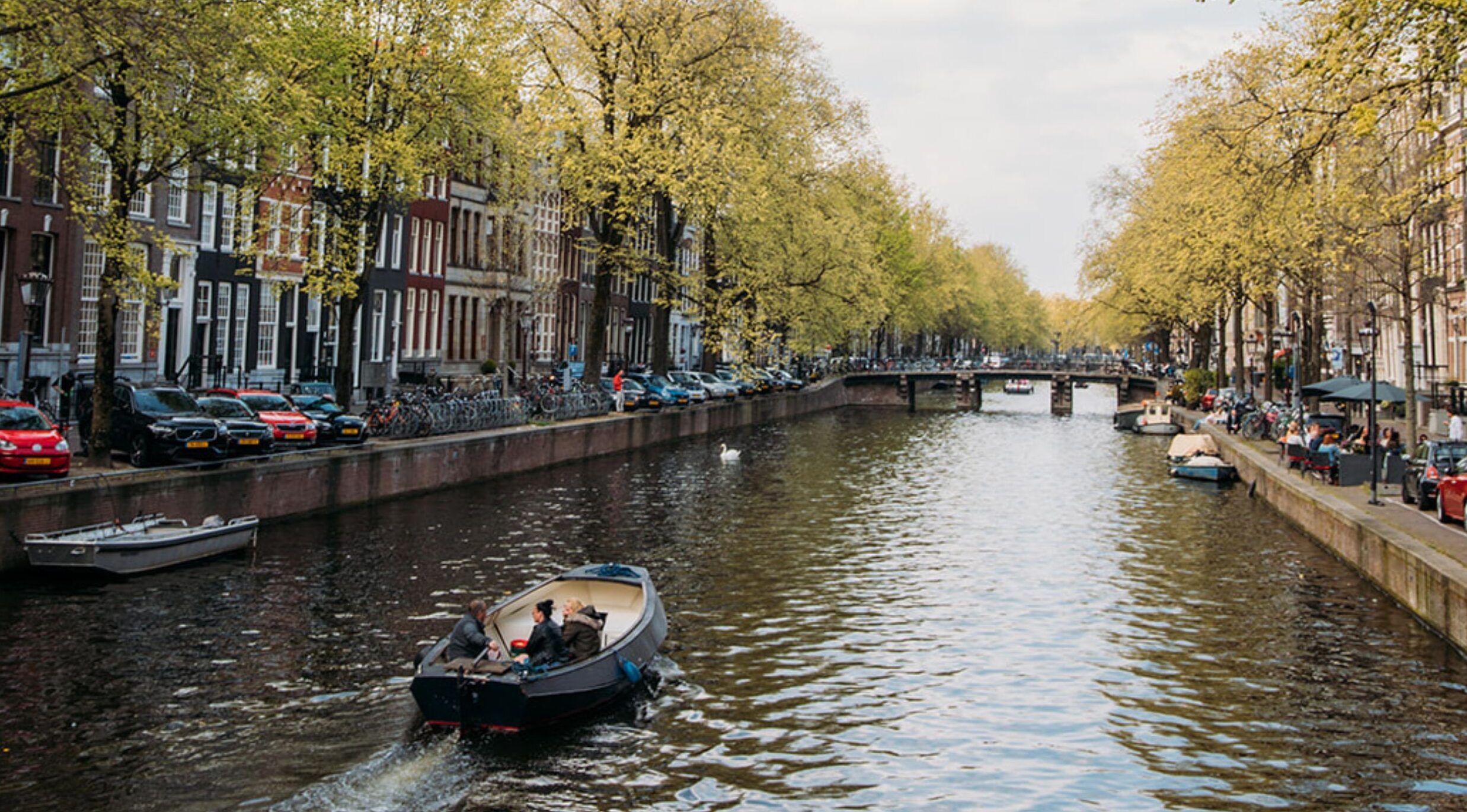 Historic canal houses along the herengracht with a boat passing by.